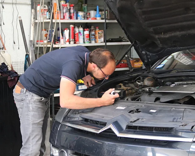 garagiste vérifiant le moteur d'une voiture, éclairant avec une lampe de poche à Gargenville près de Mantes‑la‑Jolie dans les Yvelines 78