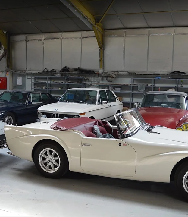 Quatre voitures classiques dans un garage : une décapotable blanche, une BMW 2002 à Gargenville près de Mantes‑la‑Jolie dans les Yvelines 78