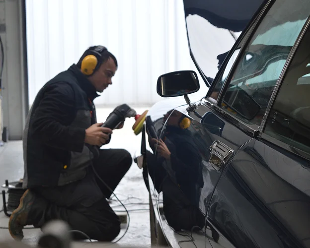 carrossier polit une voiture noire à genoux, portant un casque anti-bruit à Gargenville près de Mantes-la-Jolie dans les Yvelines 78