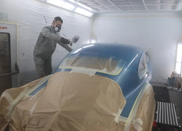 Peintre en combinaison et masque, pulvérisant de la peinture bleue sur une voiture à Gargenville près de Mantes-la-Jolie dans les Yvelines 78